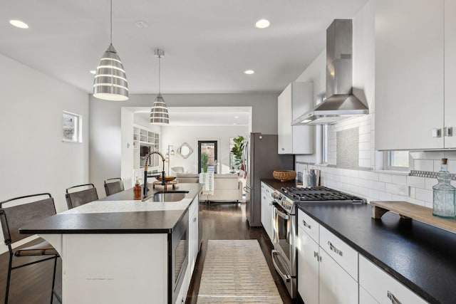 kitchen featuring white cabinetry, wall chimney exhaust hood, a breakfast bar area, a center island with sink, and appliances with stainless steel finishes