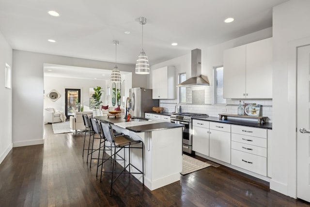 kitchen with pendant lighting, a kitchen island with sink, white cabinets, wall chimney exhaust hood, and stainless steel appliances