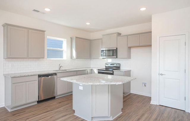 kitchen with sink, a center island, appliances with stainless steel finishes, dark hardwood / wood-style floors, and light stone countertops