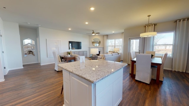 kitchen with a kitchen island, dark hardwood / wood-style floors, decorative light fixtures, white cabinetry, and light stone countertops