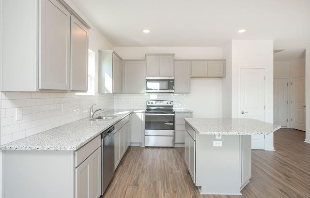 kitchen with sink, appliances with stainless steel finishes, gray cabinetry, a center island, and light stone countertops