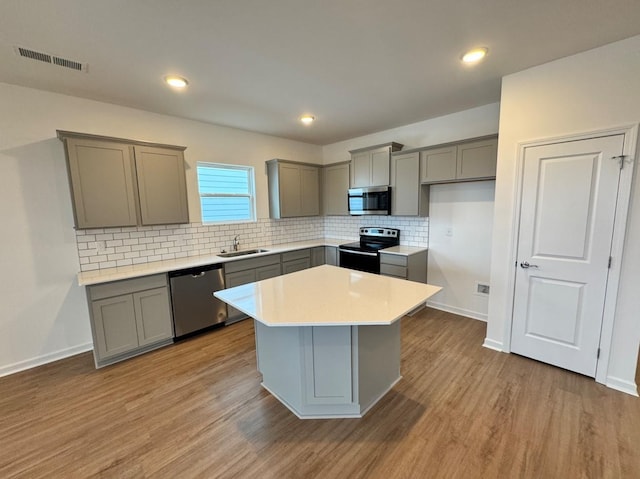 kitchen with appliances with stainless steel finishes, sink, gray cabinetry, a center island, and light hardwood / wood-style flooring