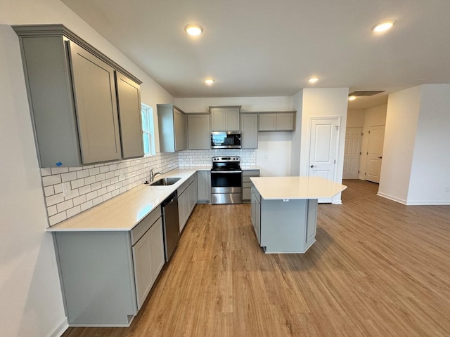 kitchen featuring gray cabinets, appliances with stainless steel finishes, a kitchen island, decorative backsplash, and light wood-type flooring