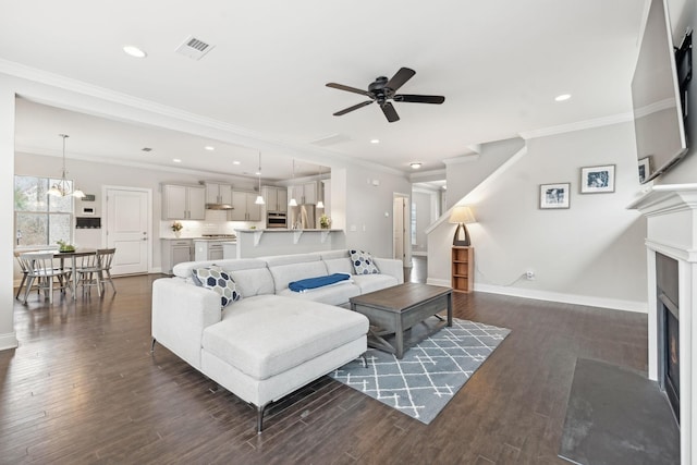 living room featuring ceiling fan with notable chandelier, crown molding, and dark wood-type flooring