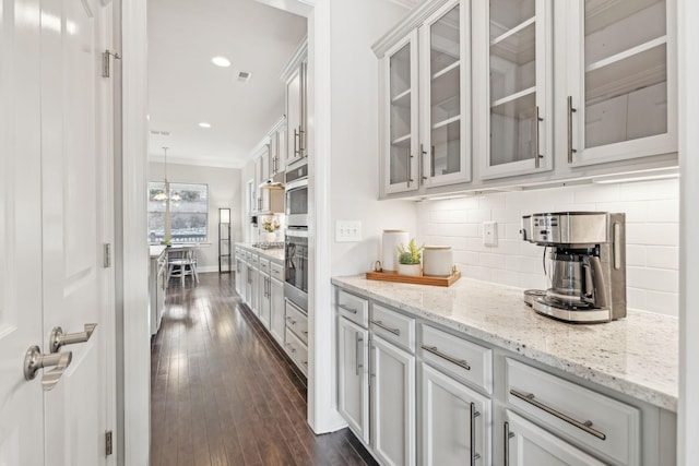 bar with light stone counters, ornamental molding, stainless steel oven, white cabinets, and dark hardwood / wood-style floors