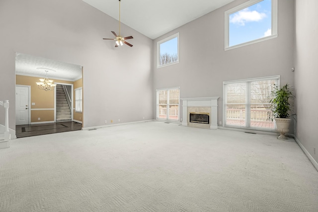 unfurnished living room featuring ceiling fan with notable chandelier, a towering ceiling, crown molding, and carpet flooring