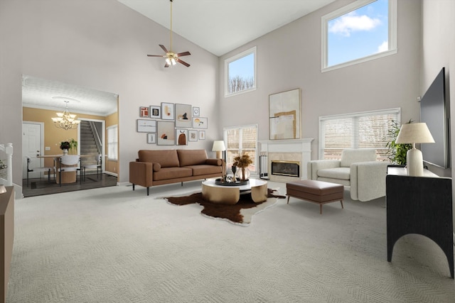 carpeted living room featuring ceiling fan with notable chandelier, a towering ceiling, and a tiled fireplace