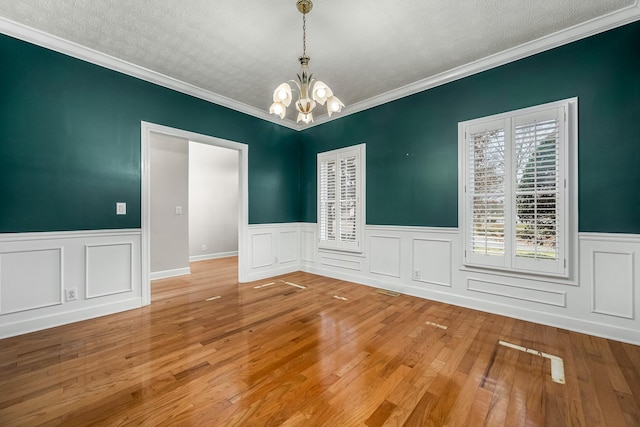 unfurnished room with crown molding, hardwood / wood-style flooring, a textured ceiling, and an inviting chandelier