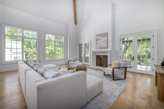 living room featuring french doors, light hardwood / wood-style flooring, beamed ceiling, and a high ceiling