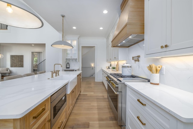 kitchen featuring premium range hood, a kitchen island with sink, white cabinets, and appliances with stainless steel finishes