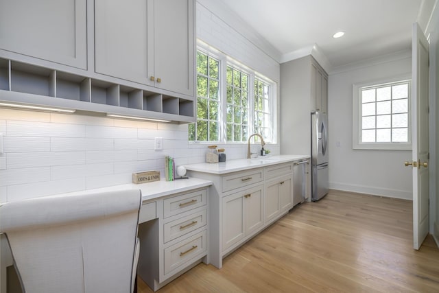 kitchen featuring appliances with stainless steel finishes, light hardwood / wood-style flooring, ornamental molding, and sink