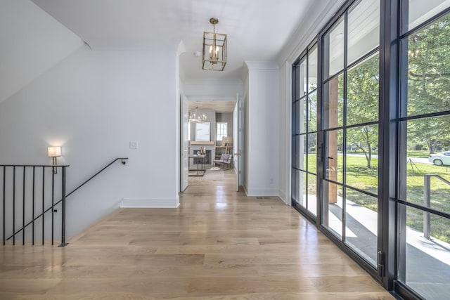 hall featuring light hardwood / wood-style flooring, ornamental molding, and a notable chandelier