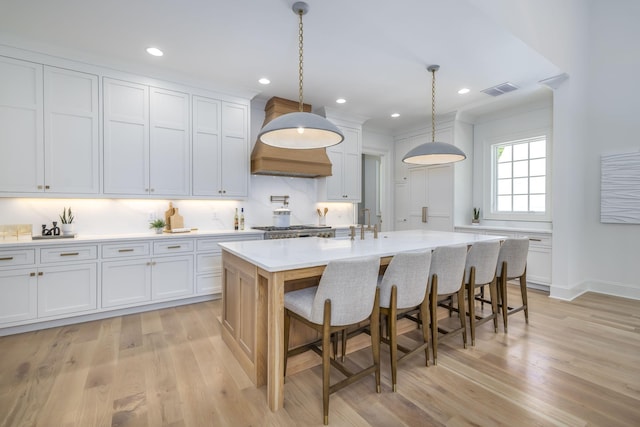 kitchen with hanging light fixtures, light hardwood / wood-style flooring, white cabinetry, and a kitchen island with sink