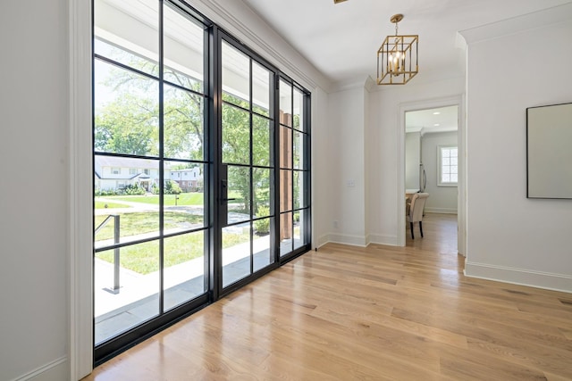 doorway with light hardwood / wood-style floors, crown molding, and a chandelier