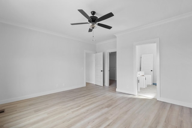 unfurnished bedroom with crown molding, baseboards, a walk in closet, light wood-style floors, and a closet