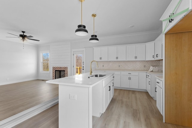 kitchen featuring backsplash, crown molding, a center island with sink, a fireplace, and a sink