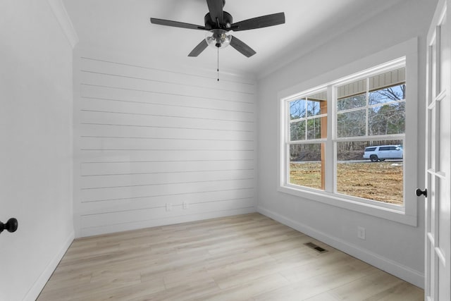 spare room featuring a wealth of natural light, visible vents, light wood-style floors, and crown molding