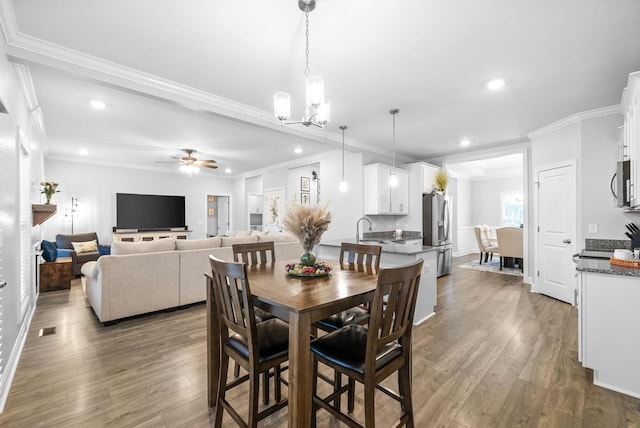 dining space with sink, ceiling fan with notable chandelier, crown molding, and dark wood-type flooring