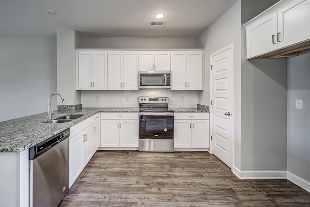 kitchen with sink, hardwood / wood-style flooring, light stone countertops, white cabinetry, and stainless steel appliances