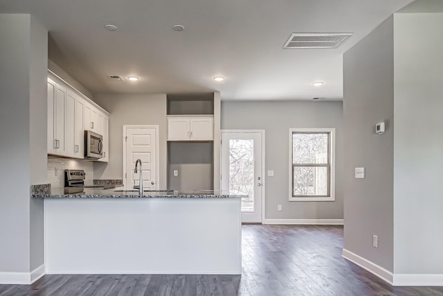 kitchen with kitchen peninsula, dark stone counters, sink, white cabinets, and range