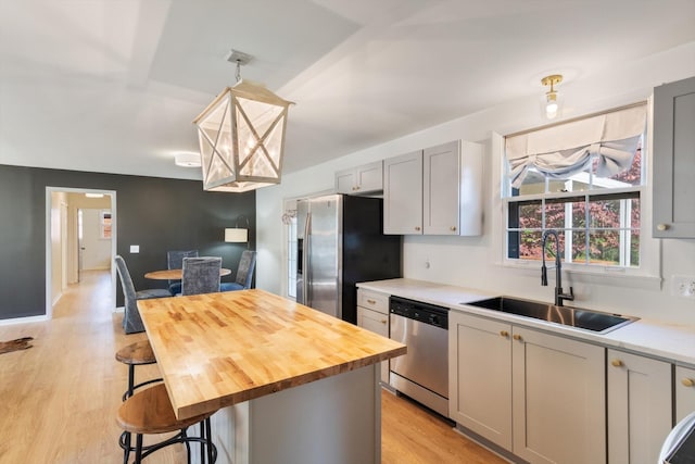 kitchen with appliances with stainless steel finishes, sink, gray cabinets, hanging light fixtures, and a breakfast bar area