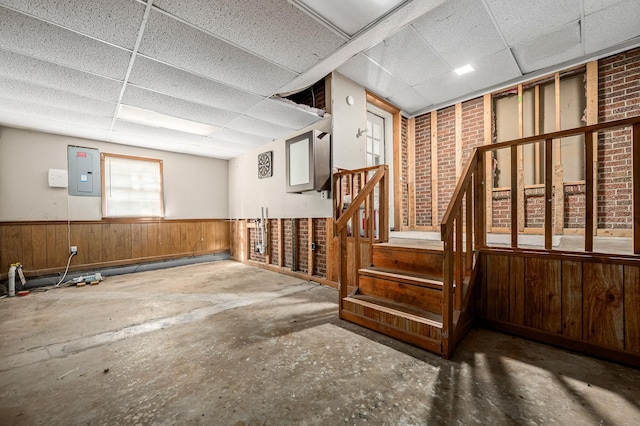 misc room with a paneled ceiling, electric panel, concrete floors, and wood walls