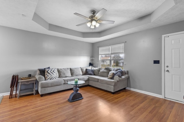 living room featuring ceiling fan, a raised ceiling, wood-type flooring, and a textured ceiling