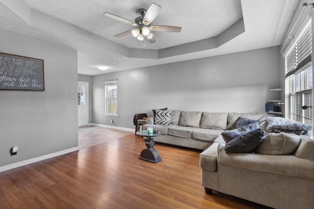 living room with hardwood / wood-style flooring, ceiling fan, plenty of natural light, and a tray ceiling