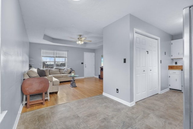 living room featuring light wood-type flooring, a tray ceiling, and ceiling fan