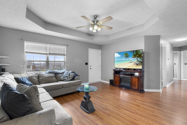 living room featuring a textured ceiling, hardwood / wood-style flooring, a raised ceiling, and ceiling fan