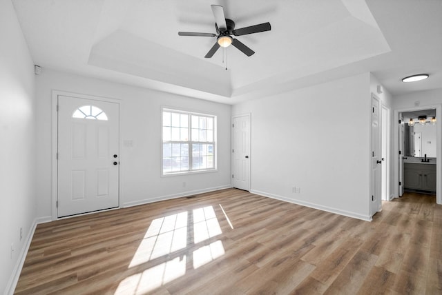 foyer with ceiling fan, a tray ceiling, and light hardwood / wood-style flooring