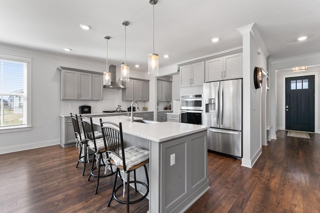 kitchen with gray cabinetry, sink, hanging light fixtures, wall chimney range hood, and appliances with stainless steel finishes