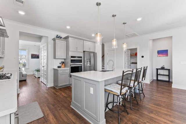 kitchen featuring gray cabinetry, hanging light fixtures, a breakfast bar area, a kitchen island with sink, and appliances with stainless steel finishes