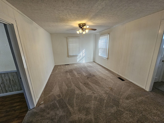 empty room featuring dark colored carpet, ceiling fan, a textured ceiling, and wooden walls