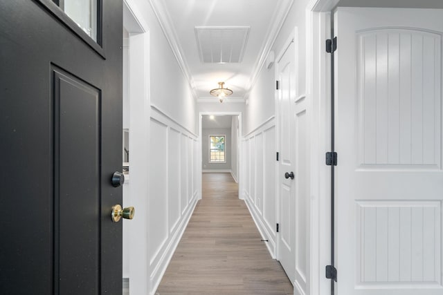 hallway featuring ornamental molding, visible vents, a decorative wall, and light wood-style flooring