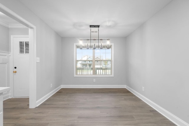 unfurnished dining area with a chandelier, wood finished floors, and baseboards