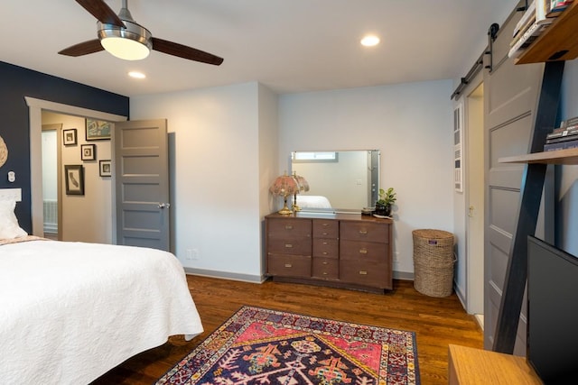 bedroom with dark hardwood / wood-style flooring, a barn door, and ceiling fan