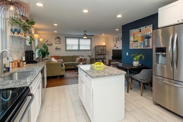 kitchen with stainless steel refrigerator with ice dispenser, light stone counters, a kitchen island, sink, and white cabinetry