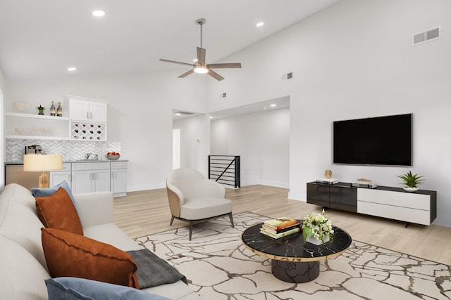 living room with ceiling fan, light hardwood / wood-style floors, sink, and high vaulted ceiling