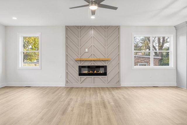 unfurnished living room with light wood-type flooring, a large fireplace, and ceiling fan