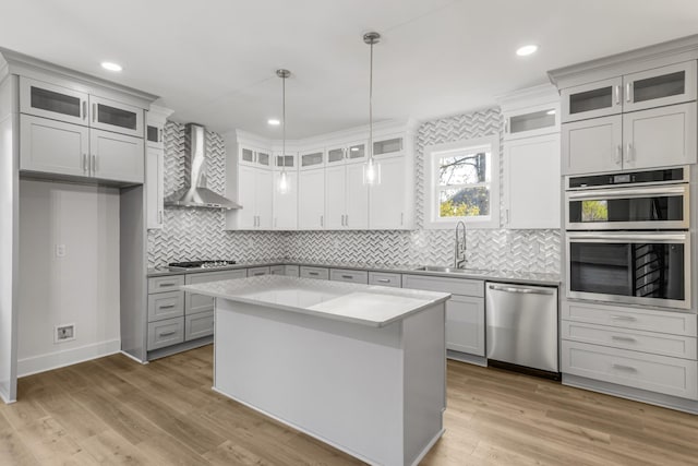 kitchen featuring appliances with stainless steel finishes, wall chimney exhaust hood, sink, a kitchen island, and hanging light fixtures