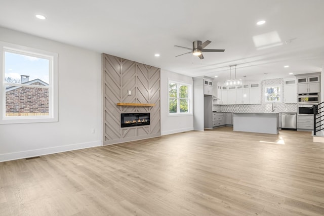 unfurnished living room with a large fireplace, light hardwood / wood-style flooring, ceiling fan, and sink