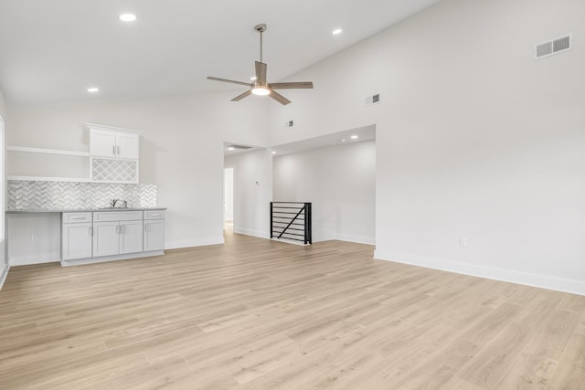 unfurnished living room with high vaulted ceiling, light hardwood / wood-style flooring, ceiling fan, and sink