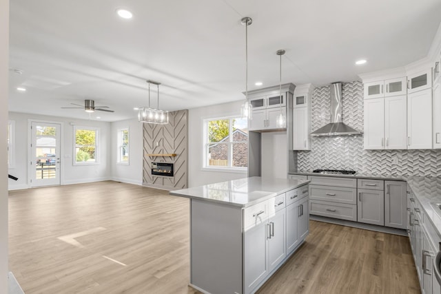 kitchen featuring ceiling fan, wall chimney exhaust hood, hanging light fixtures, gray cabinets, and a kitchen island