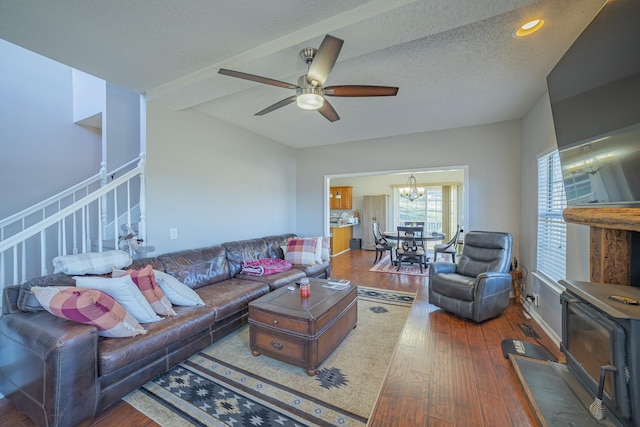 living room with ceiling fan with notable chandelier, hardwood / wood-style floors, a textured ceiling, and a wood stove