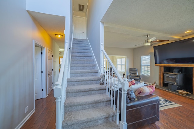 stairs featuring a textured ceiling, hardwood / wood-style flooring, a wood stove, and ceiling fan