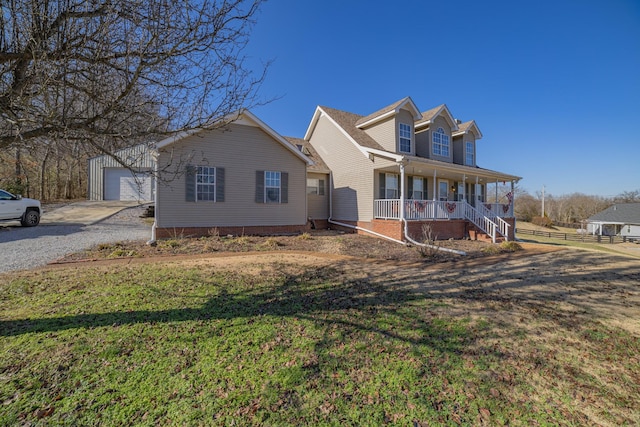 new england style home featuring a front yard, a porch, an outbuilding, and a garage