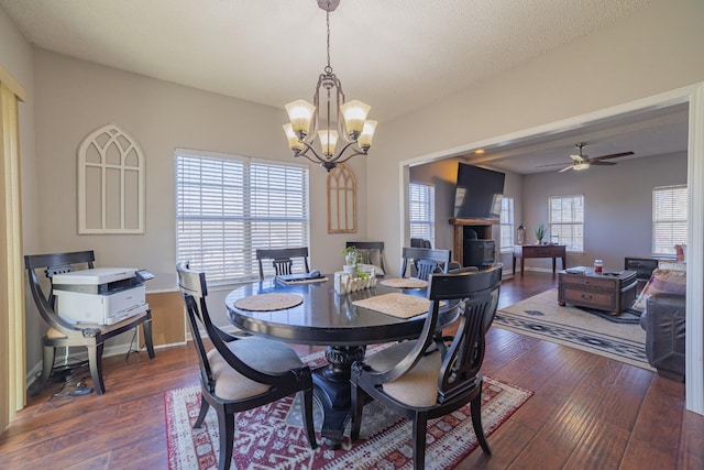 dining space with a healthy amount of sunlight, ceiling fan with notable chandelier, a textured ceiling, and dark wood-type flooring