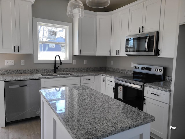 kitchen featuring a sink, light stone counters, a kitchen island, white cabinetry, and appliances with stainless steel finishes