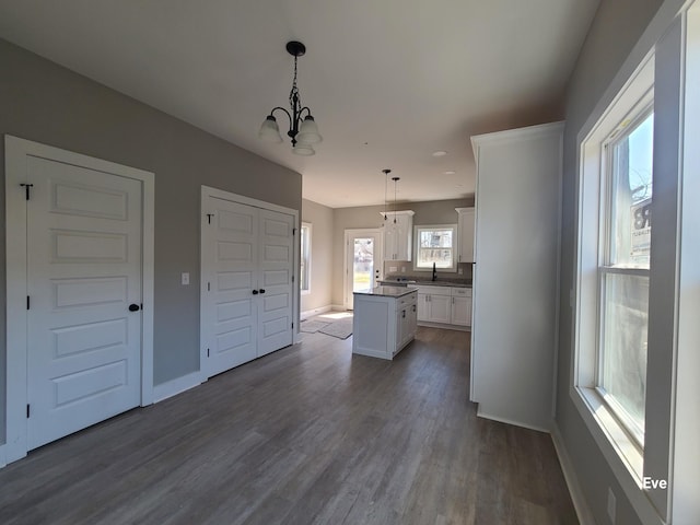 kitchen with a center island, dark wood finished floors, decorative light fixtures, white cabinets, and a sink